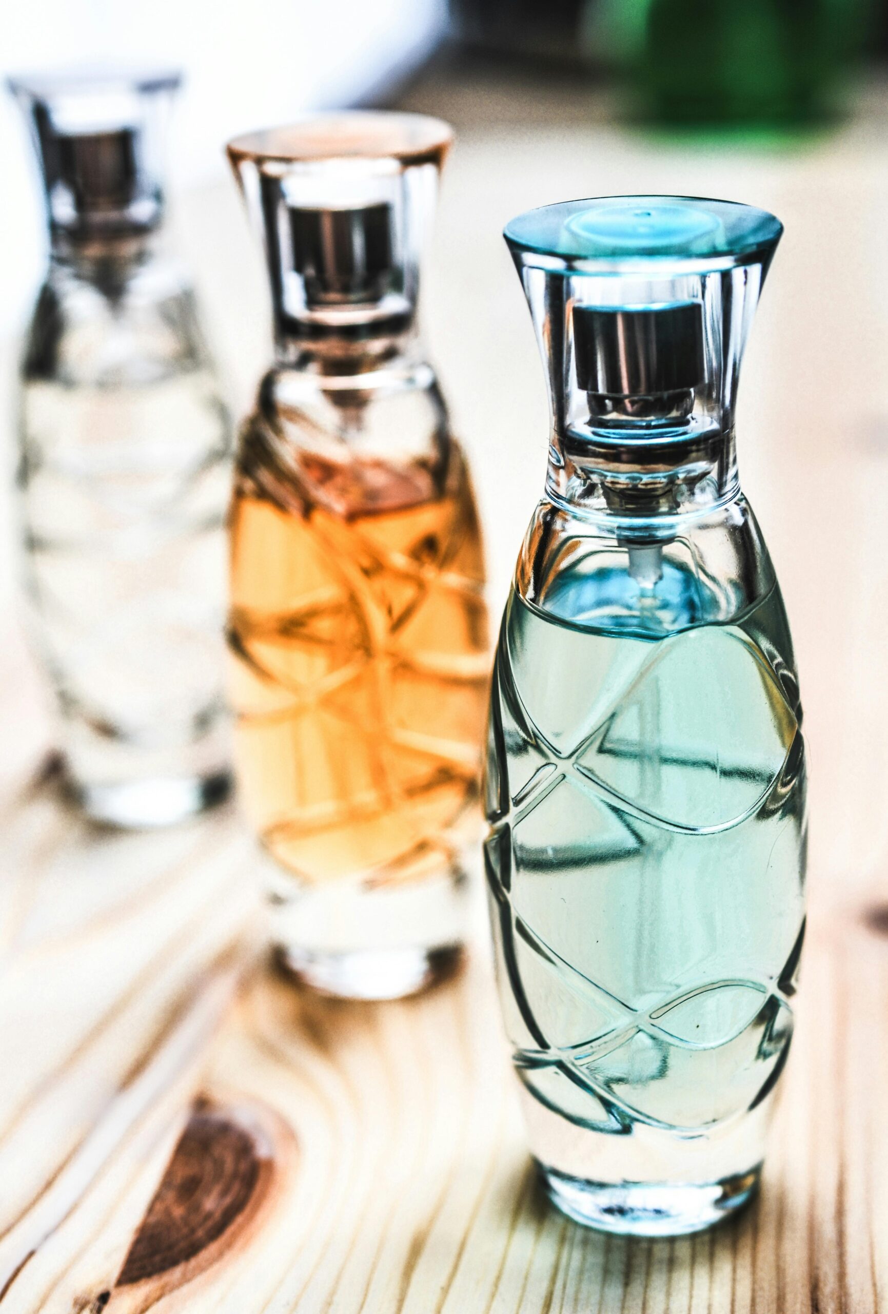 Artistic shot of elegant perfume bottles with colorful liquids on a wooden surface.